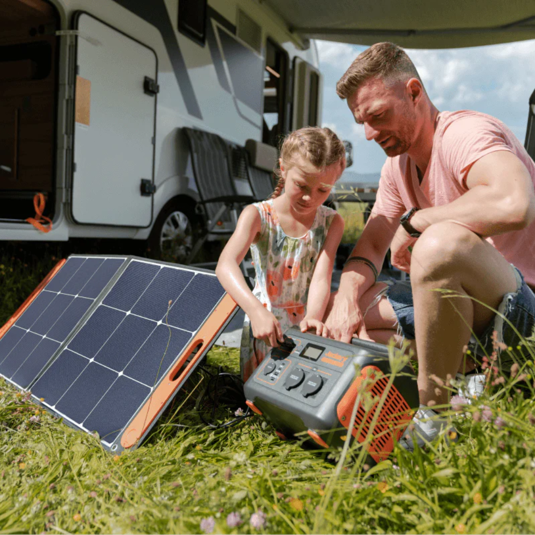 Man and child with a portable power station and solar panel near an RV.