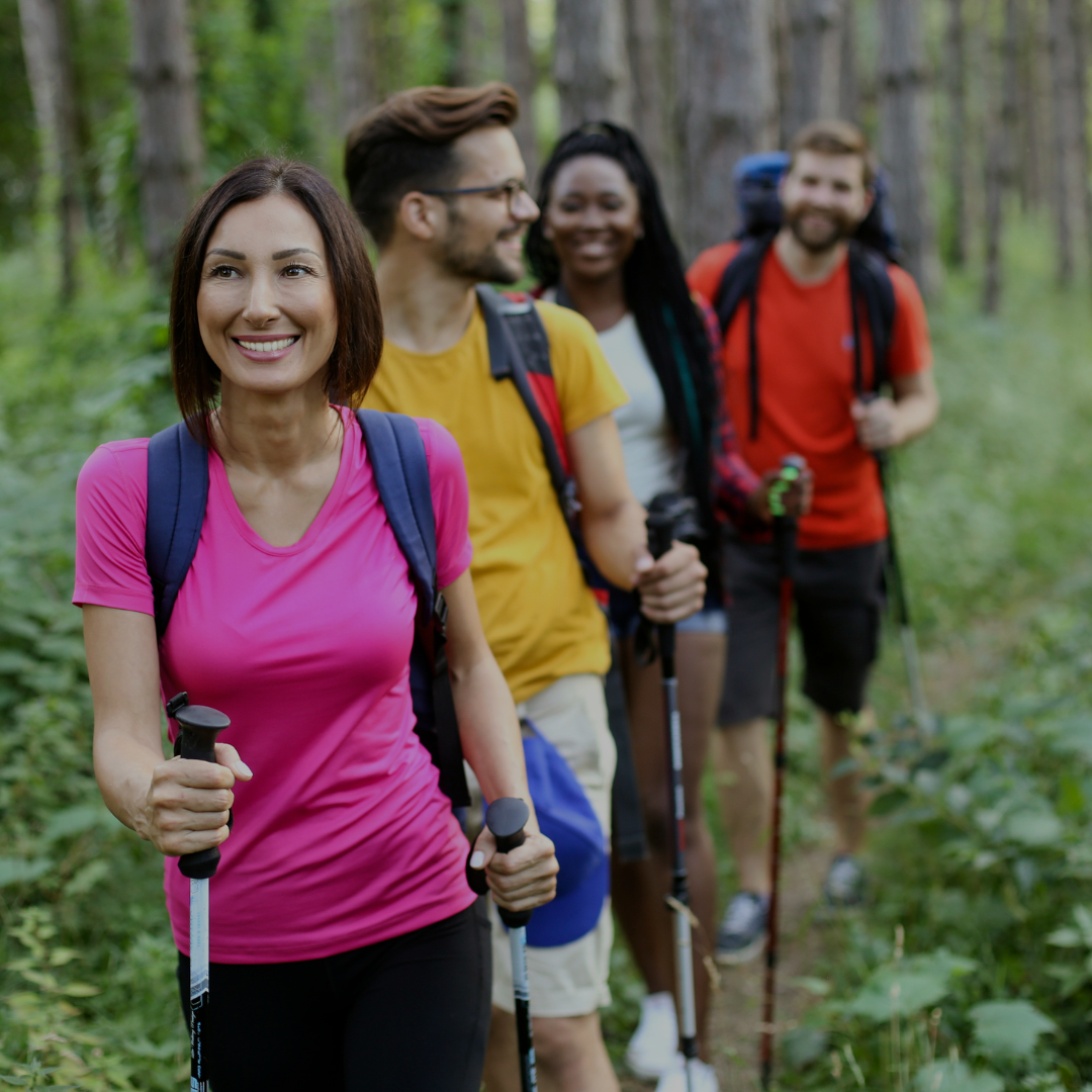 Group of four friends hiking in a forest, smiling and enjoying their time outdoors.