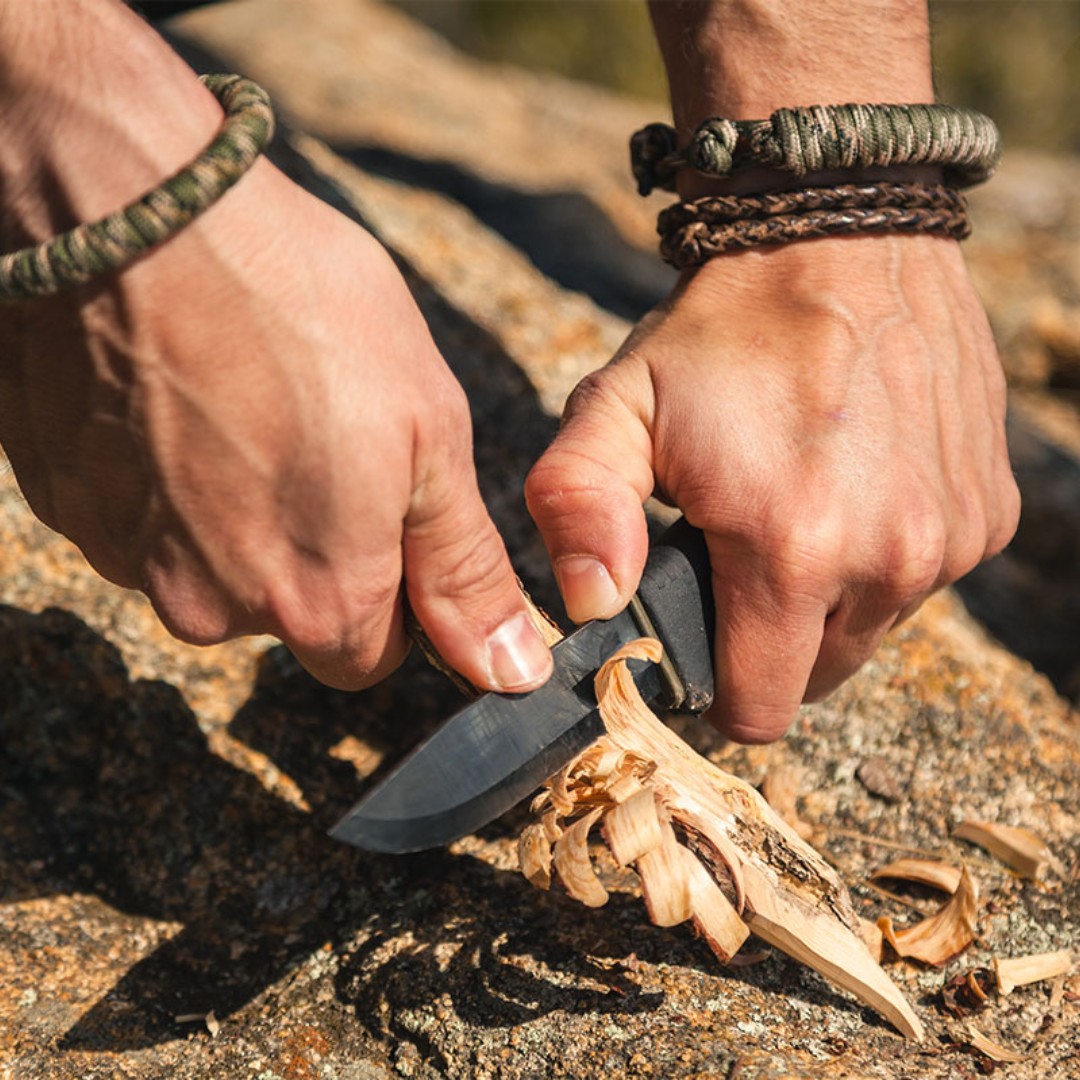 Person using a knife to peel wood on a natural background