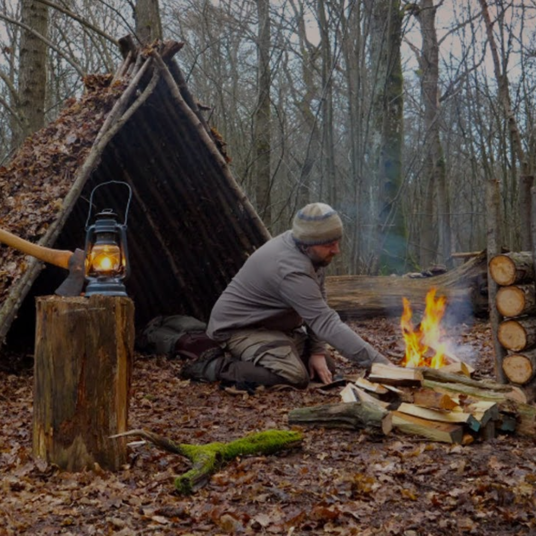 Person by a campfire in front of a makeshift shelter in the woods