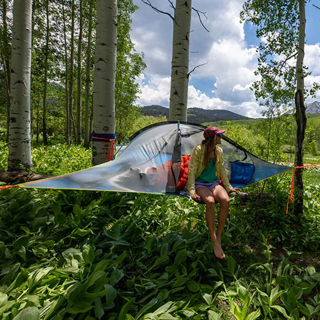 Person sitting on a tree tent in a forested area with mountains in the background